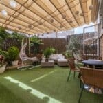 Terrace of a house with artificial grass floors, tables, outdoor seating, lots of plants and an extended retractable awning