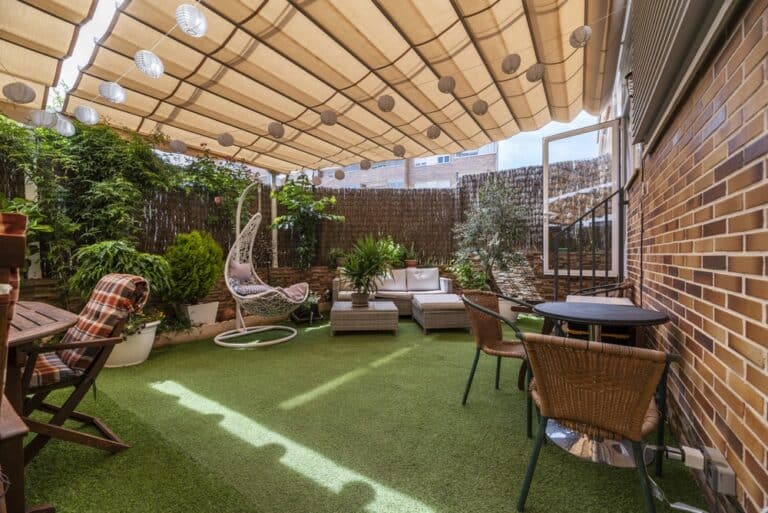 Terrace of a house with artificial grass floors, tables, outdoor seating, lots of plants and an extended retractable awning