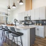 large working chefs kitchen with long white granite counter top hardwood floors grey cabinets stainless appliances large view windows dining table set for dinner